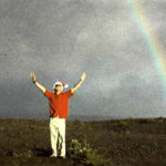 Chris Campbell raising arms triumphantly next to a rainbow